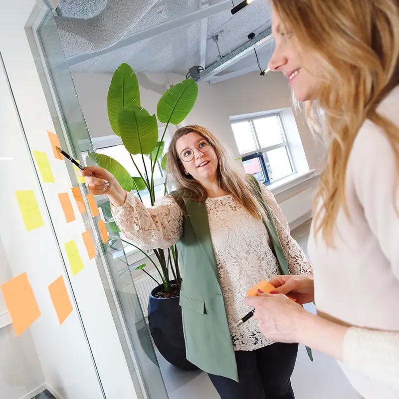 Nanda en Judith vergaderen bij het raam met post-its